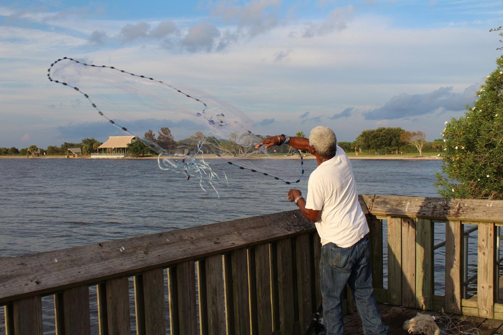 Man throwing a fishing net off a pier.