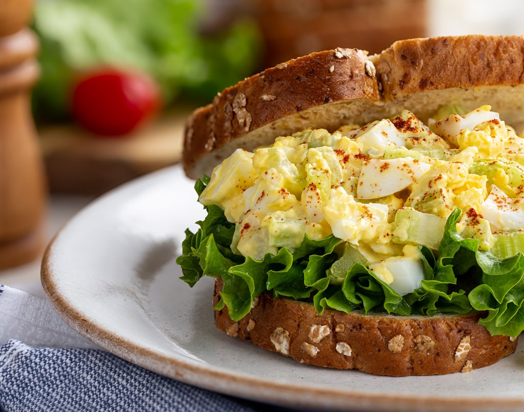 Closeup of egg salad sandwich on whole grain bread on a plate.