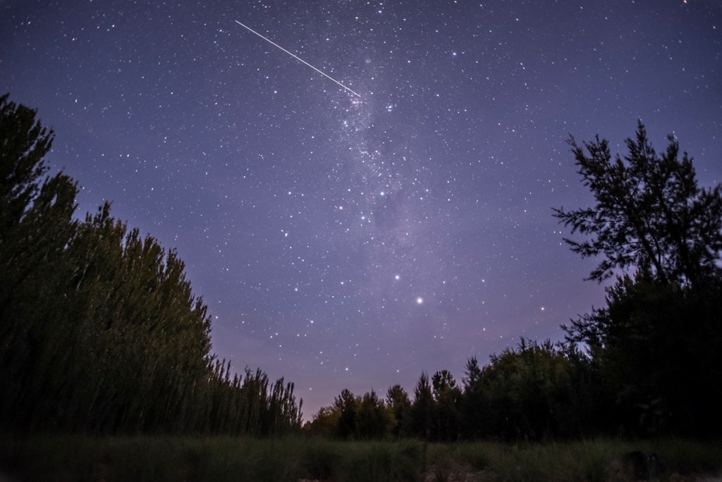 A dark and star-filled sky is crossed by a meteor with a long tail.
