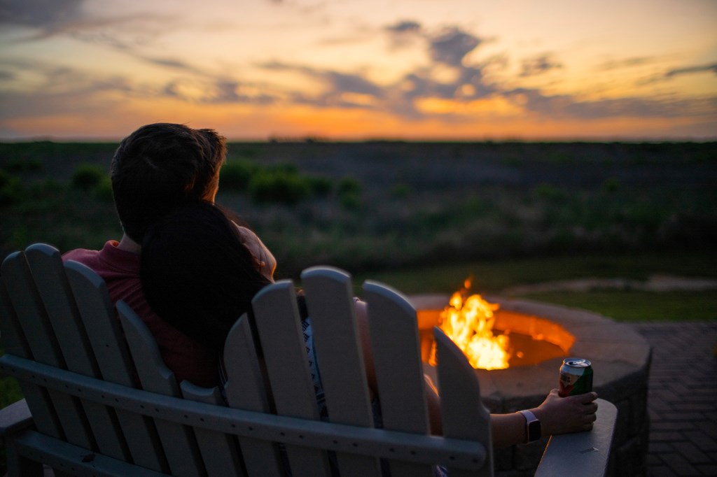 A couple looks at the sunset while enjoying a campfire.